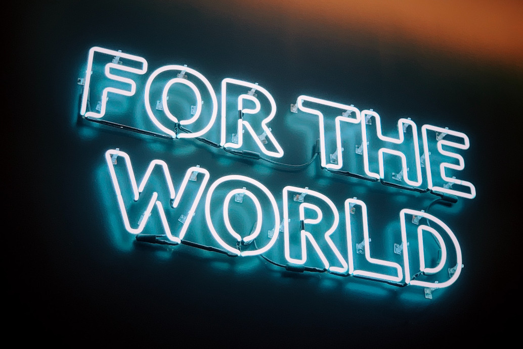 Neon sign displaying the words "for the world" against a dark background.